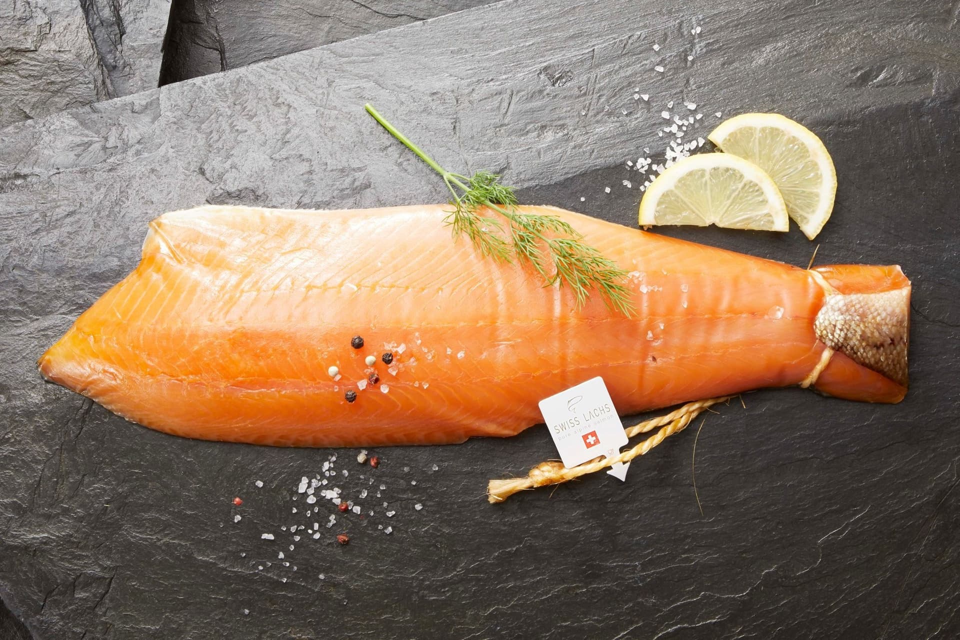 Ganze geräucherte Lachsseite mit Dill, Pfeffer und Zitrone auf einer Schieferplatte