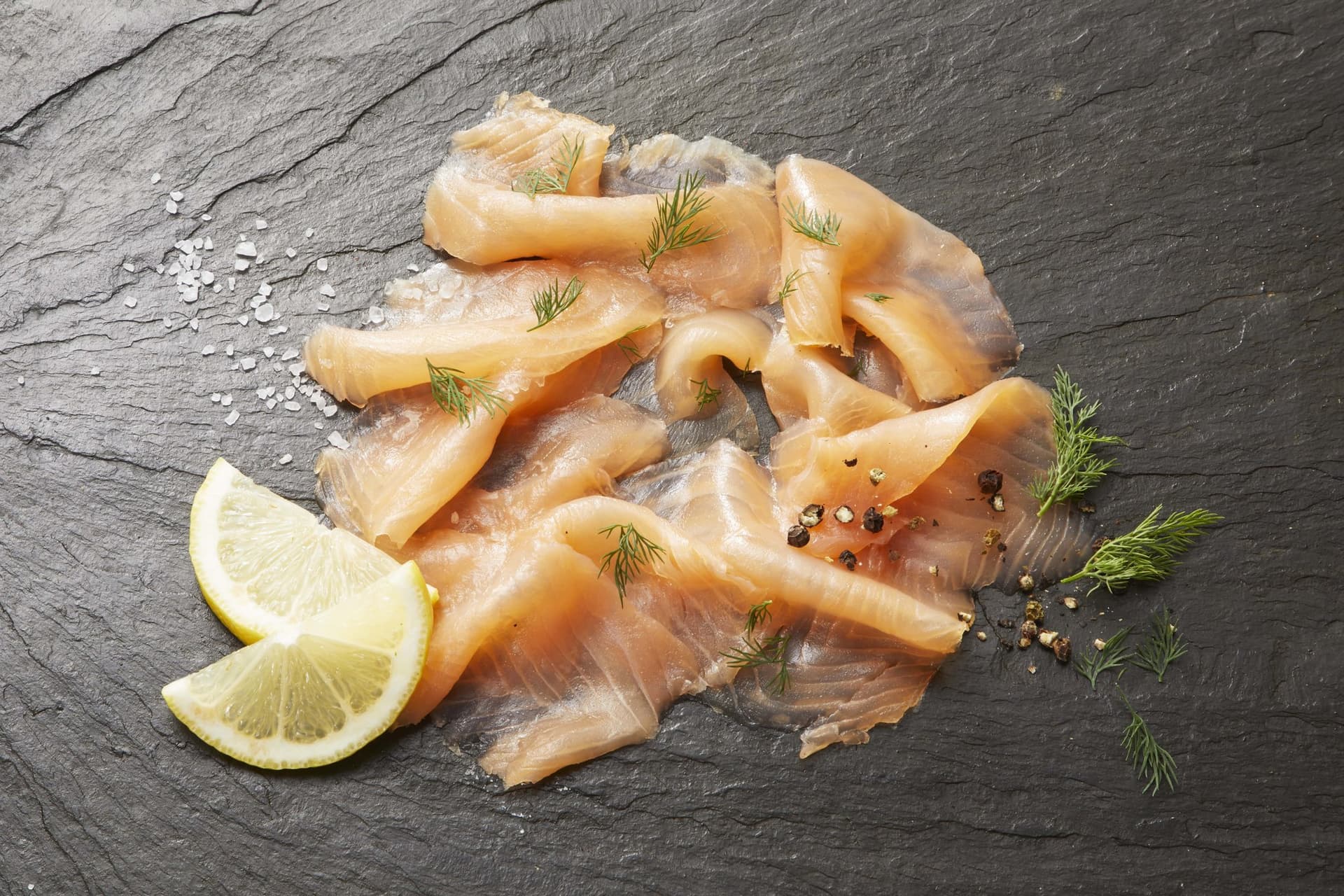 Geräucherter Lachs in feinen Tranchen auf Schiefer, mit Dill, Zitrone, Salz und Pfeffer