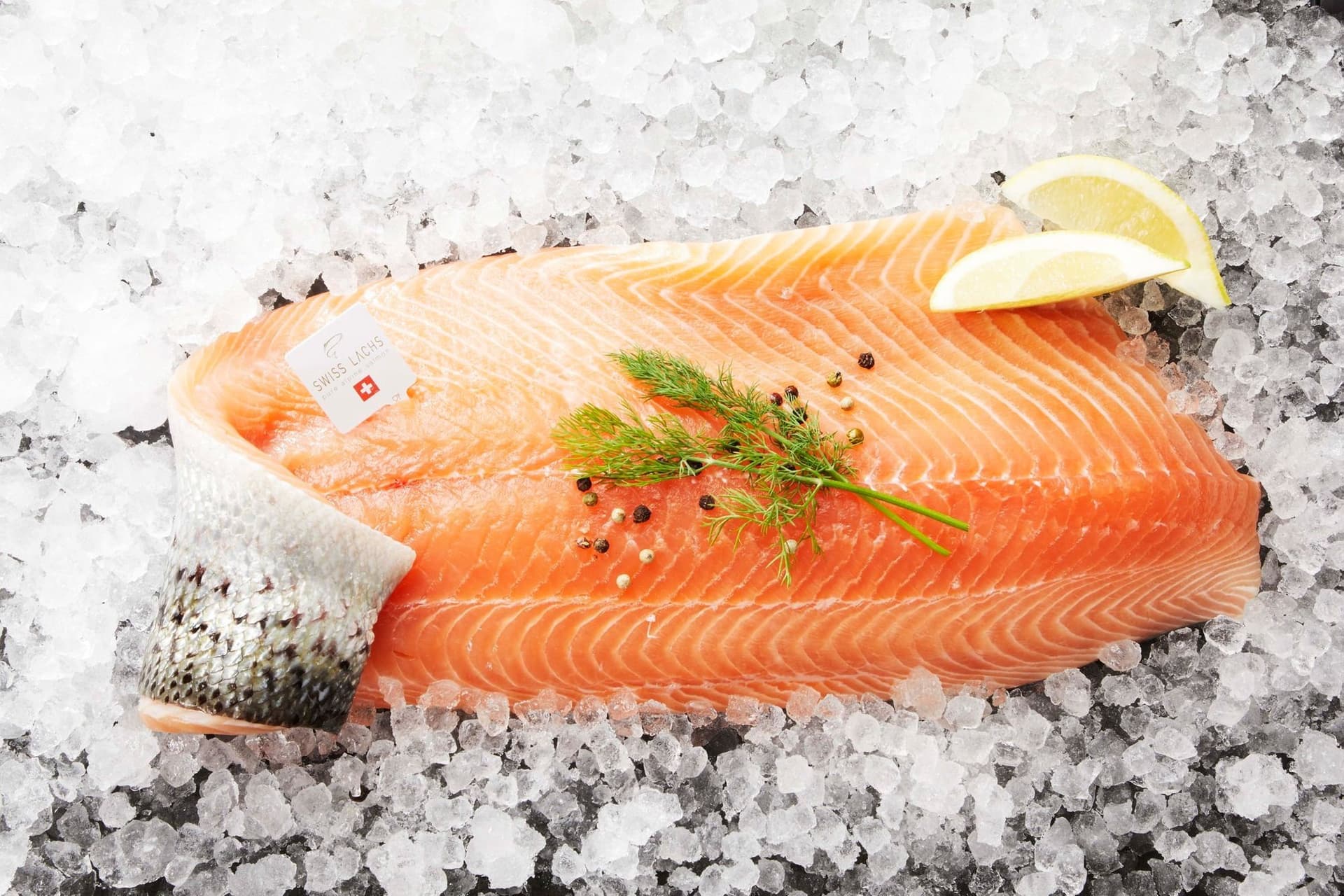 Frische Lachsseite mit Haut auf Crushed Ice, mit dem Etikett von Swiss Lachs, Dill und Zitrone